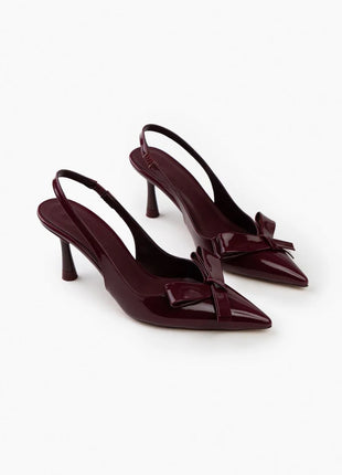 Bordo LUCINDA Slingback-Pumps aus glänzendem Lackleder mit spitzer Vorderkappe, mittelhohem schmalen Absatz und verstellbarem Slingback-Riemen. Dekorative Schleife auf der Vorderseite.