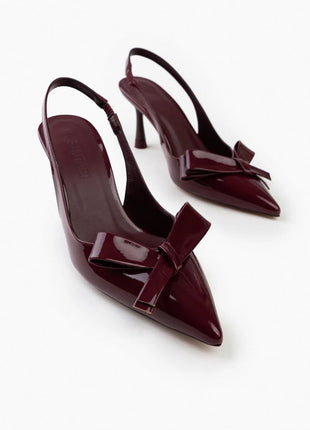 Bordo LUCINDA Slingback-Pumps aus glänzendem Lackleder mit spitzer Vorderkappe, mittelhohem schmalen Absatz und verstellbarem Slingback-Riemen. Dekorative Schleife auf der Vorderseite.