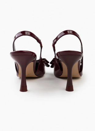 Bordo LUCINDA Slingback-Pumps aus glänzendem Lackleder mit spitzer Vorderkappe, mittelhohem schmalen Absatz und verstellbarem Slingback-Riemen. Dekorative Schleife auf der Vorderseite.