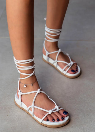 Weiße PERRY Sandalen mit flacher Sohle und eleganten Schnürdetails, die um den Knöchel gebunden werden. Komfortables und trendiges Design für den Sommer.