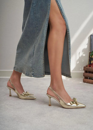 Goldene LUCINDA Slingback-Pumps aus glänzendem Lackleder mit spitzer Vorderkappe, mittelhohem schmalen Absatz und verstellbarem Slingback-Riemen. Dekorative Schleife auf der Vorderseite.