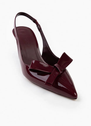 Bordo LUCINDA Slingback-Pumps aus glänzendem Lackleder mit spitzer Vorderkappe, mittelhohem schmalen Absatz und verstellbarem Slingback-Riemen. Dekorative Schleife auf der Vorderseite.