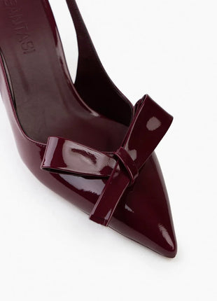 Bordo LUCINDA Slingback-Pumps aus glänzendem Lackleder mit spitzer Vorderkappe, mittelhohem schmalen Absatz und verstellbarem Slingback-Riemen. Dekorative Schleife auf der Vorderseite.